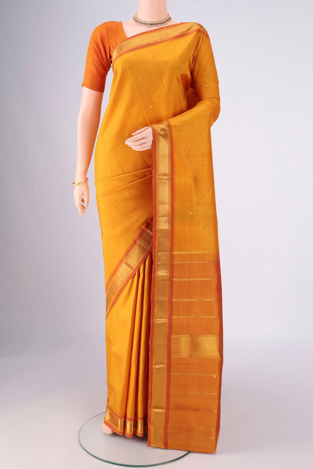 Mustard Kanchipuram Silk Saree with Zari Butta on the body and Zari Border.  displayed on a mannequin