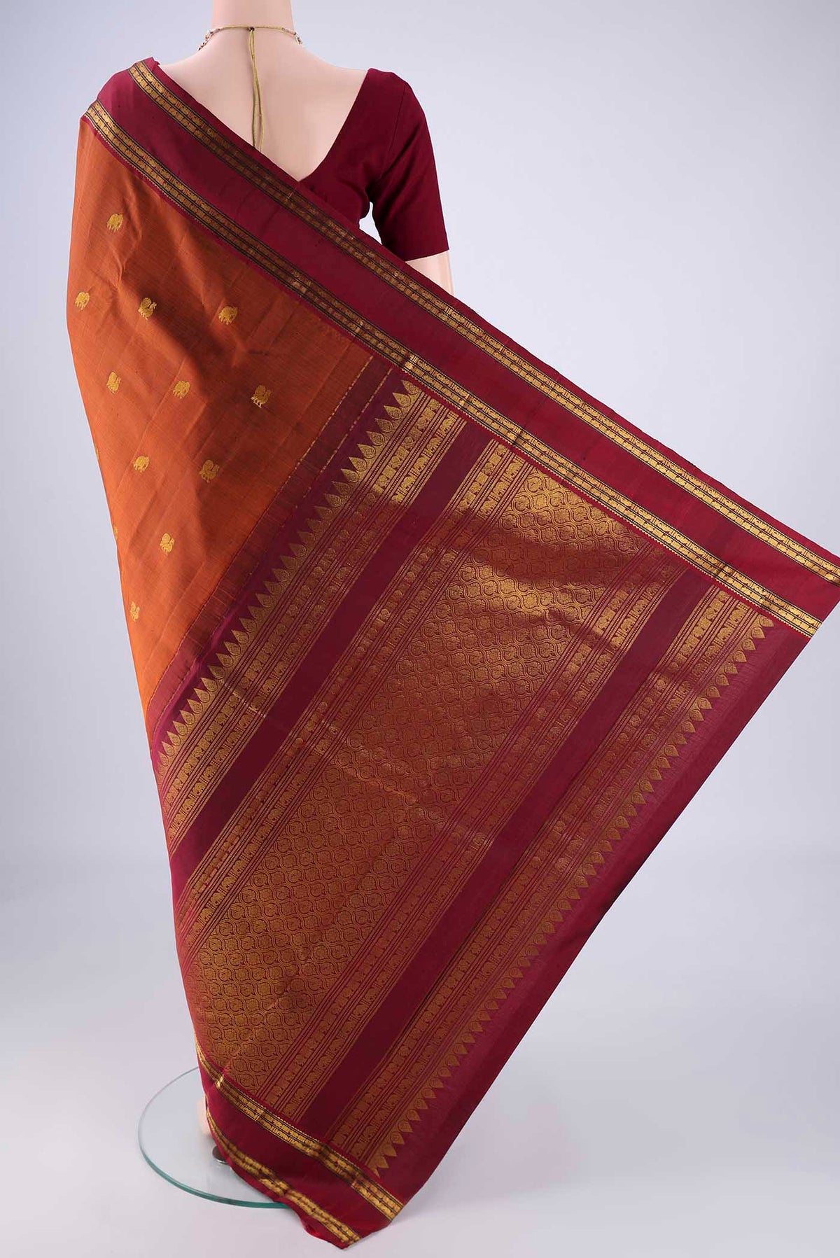 Flat view of Rust Kanchipuram Silk Saree with Zari Butta on the body and Zari Border. 