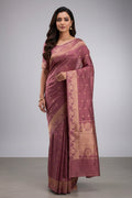 Model wearing a Gulal, handwoven in Katan silk with gold zari, is crafted using the phekwa technique, allowing closely spaced motifs to emerge with precision Tiny floral butis in a dense half-step repeat lend the body a soft, textured richness Art Nouveau?inspired floral arches define the borders, each framing a complementary buta, while a solid gold twill pallu completes the saree with depth and classic balance