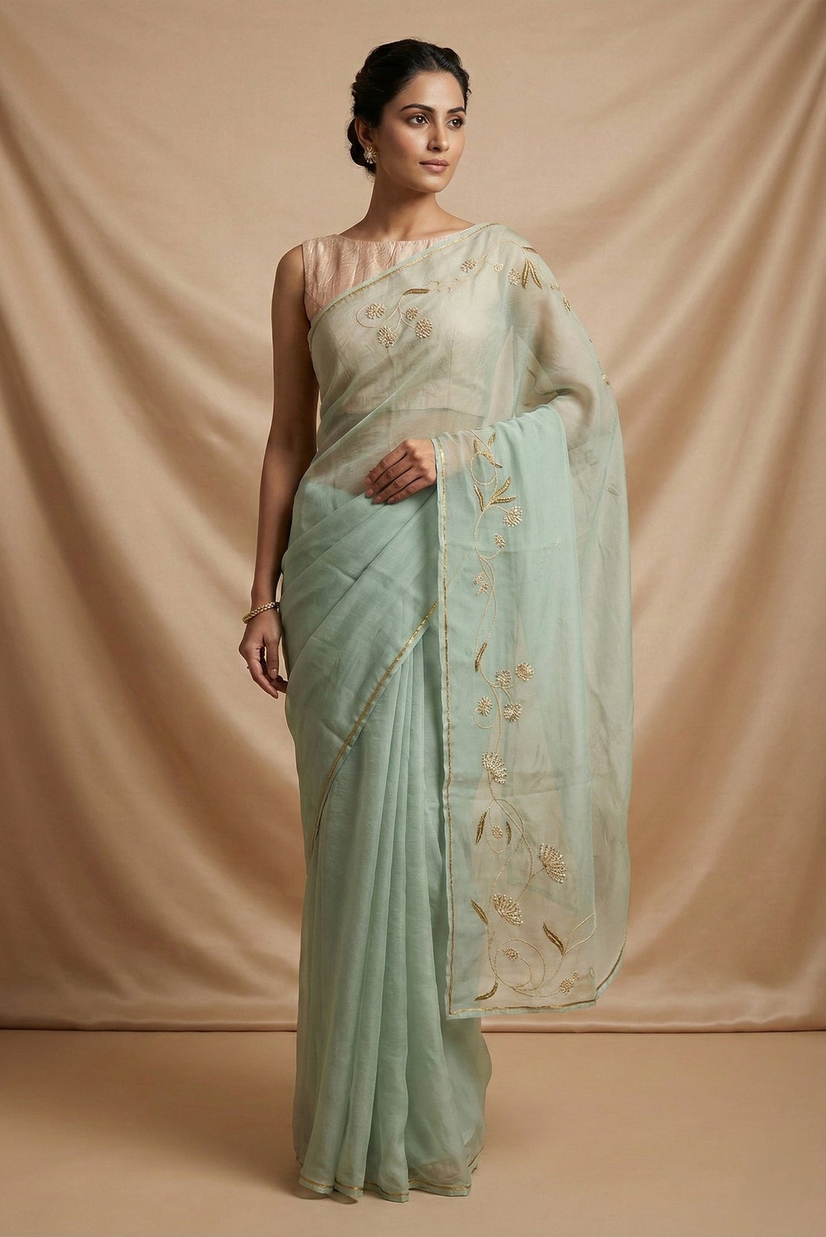Model wearing a Bahar, crafted in silk organza, features delicate pani-zari enriched with zardozi, gota work, and dabka embroidery Its defining element is an off-center floral vine running vertically through the body, breaking symmetry with quiet intent Inspired by Art Nouveau?s flowing lines, the vine is rendered in slender leaves, zari chain-stitched stems, and alternating gota and zardozi flowers The pallu trails gently onto the body in scattered embroidered blooms