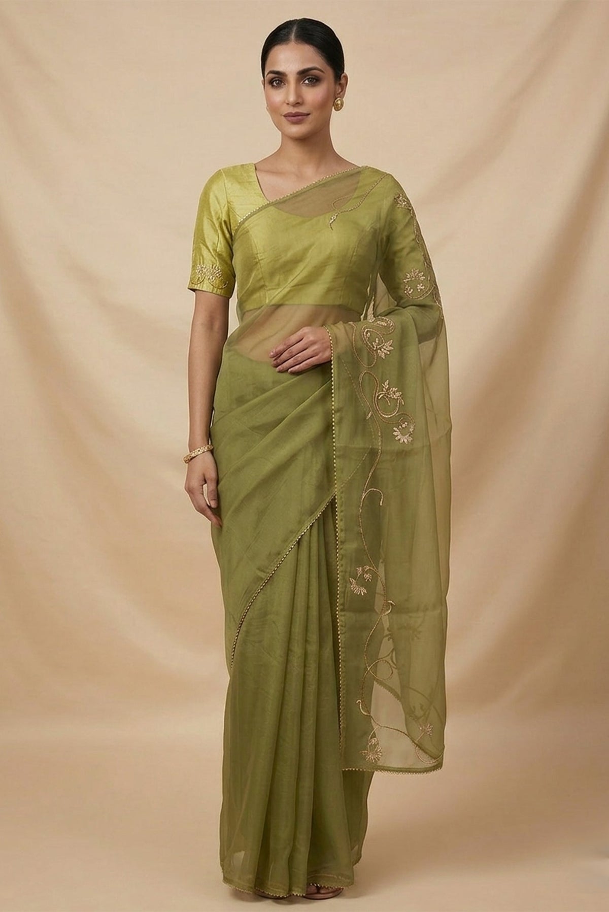 Model wearing a In Mira, pure silk organza becomes a canvas for antique gold and pani zari, brought to life through fine dabka and aari embroidery. The pallu takes inspiration from the bull masks of the Cameroon Grasslands, translating their powerful curves into graceful motifs layered with florals and Art Nouveau lines. Dual-tone zari and detailed shoulders lend the saree depth, movement, and a refined festive glow.