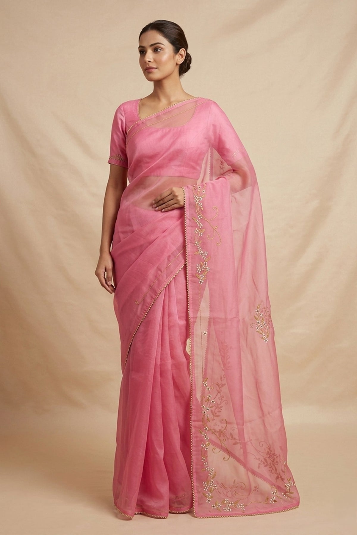 Model wearing a Mahira organza saree is inspired by the hydrangea blooms of the Art Nouveau movement. Along the border and edges, bold, simplified hydrangea blooms pair with fluid, curving stems. The flowers gain soft dimension through pani-zari zardozi, while antique-gold aari embroidery adds depth and balance. The pallu features three large asymmetrical butas, formed as flowing clusters of hydrangea blooms and stems, creating a graceful focal point.