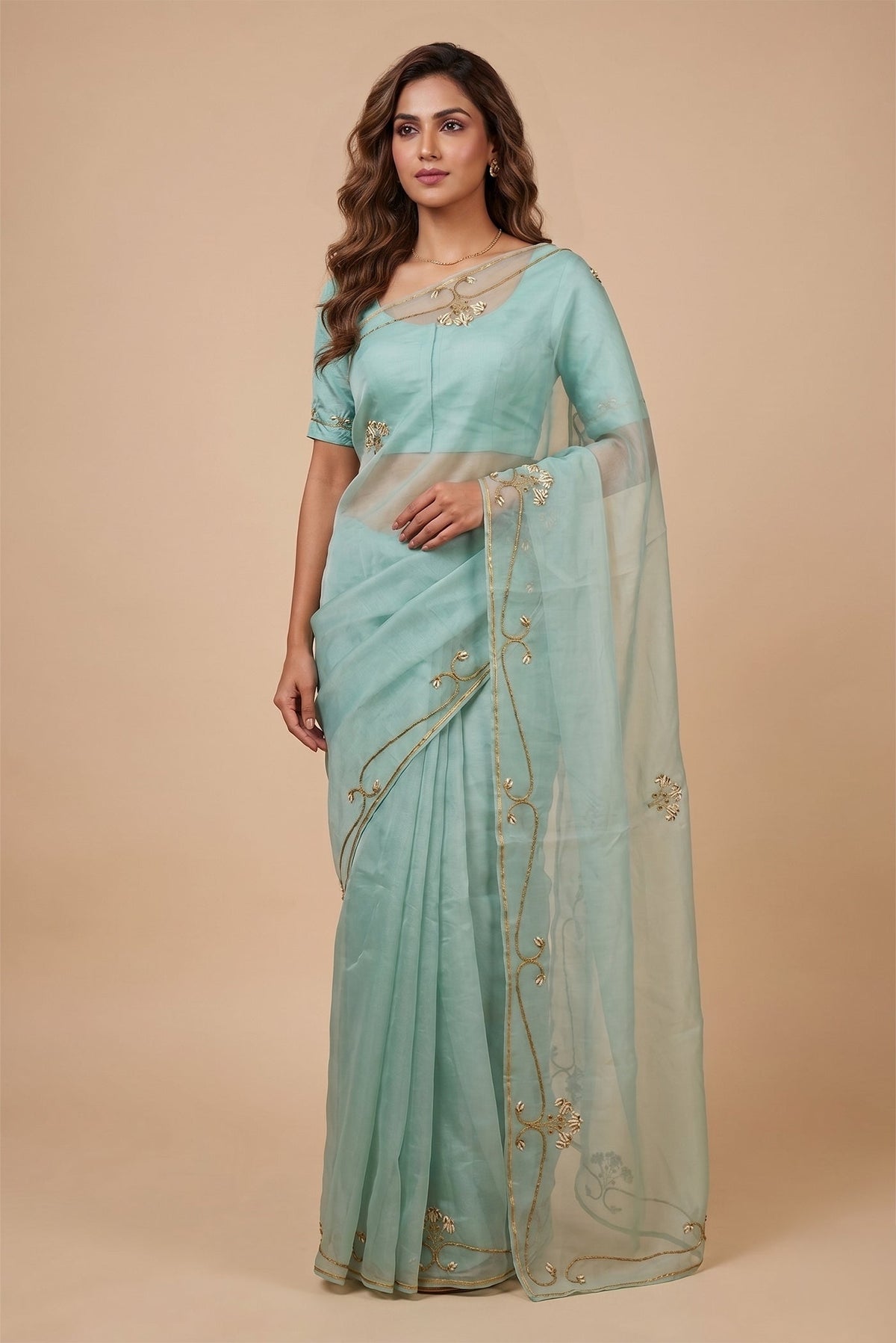 Model wearing a Meher, crafted in silk organza, is hand-embroidered with gold and antique-gold zardozi. Organic vines and floral buds form a rich border that meets at a delicate fan motif - an ornamental form celebrated in late 19th and early 20th century Art Nouveau design. Iris flowers, symbolising femininity, grace, and mystique, echo the saree?s fluid curves as the motif repeats across the body, finished with elegant gota edges.