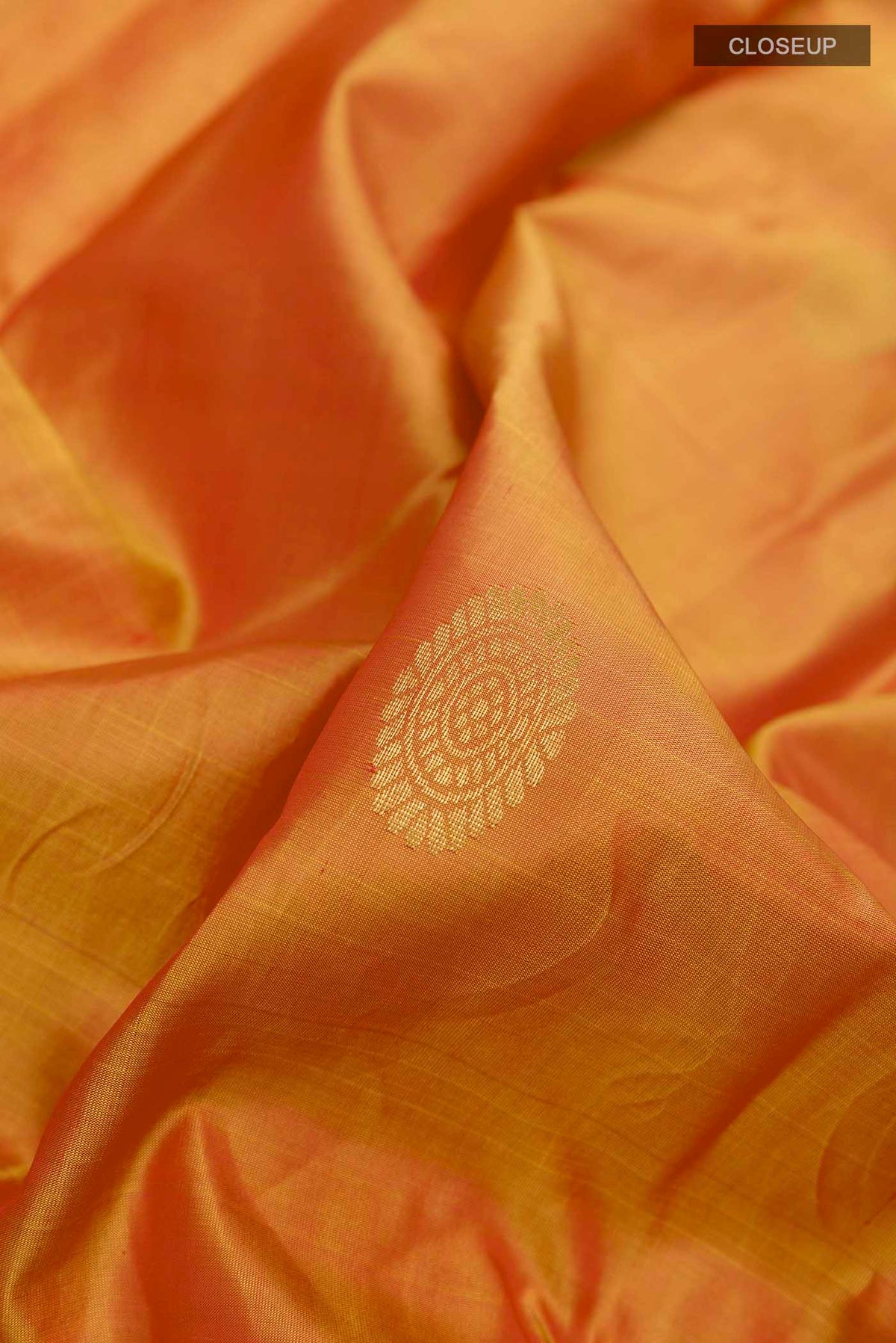 Close up of Orange Kanchipuram Silk Saree with Zari Butta on the body and Zari Border displaying folds