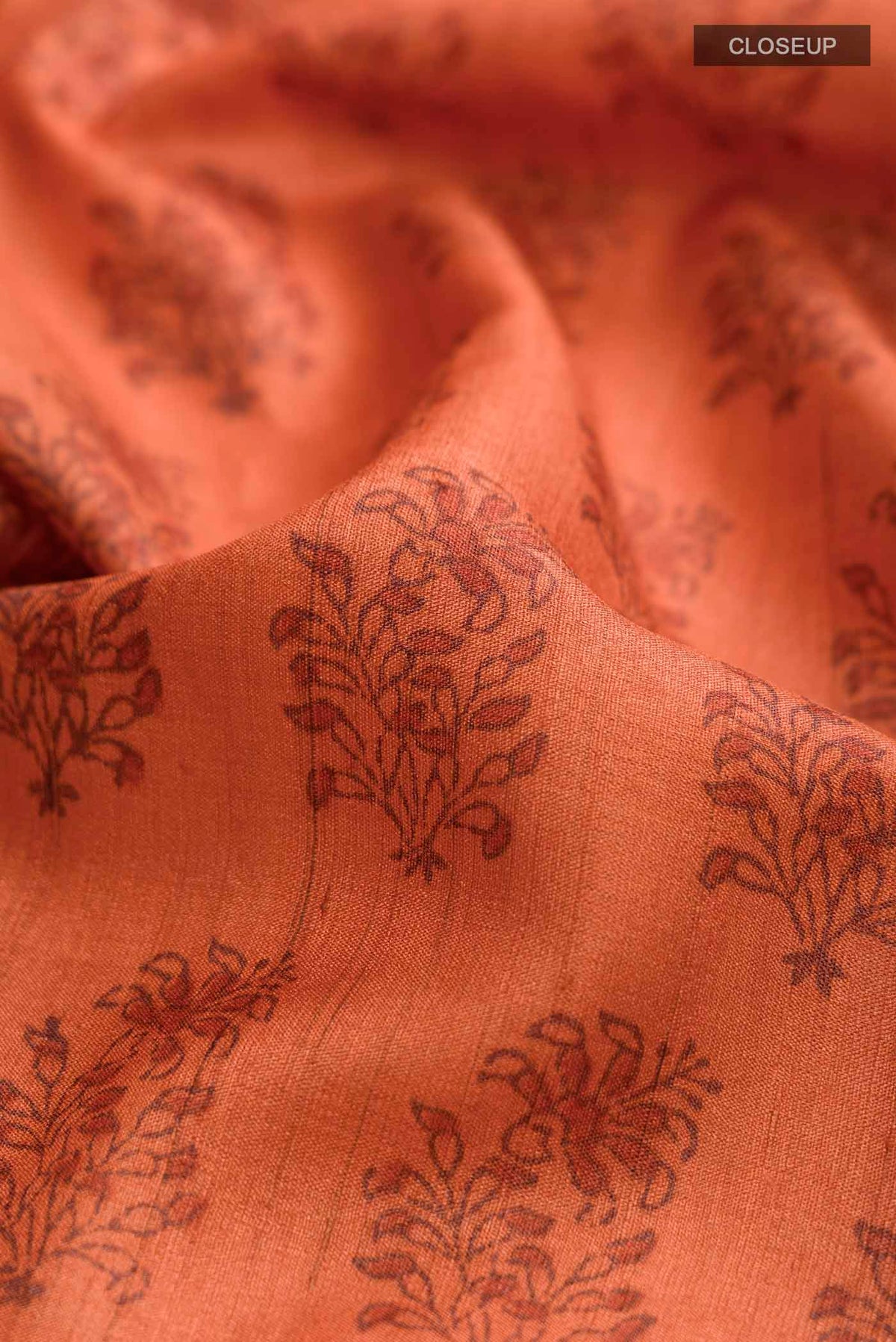 Close up of Orange Tussar Silk Saree with Printed design on the body and Plain Border displaying folds