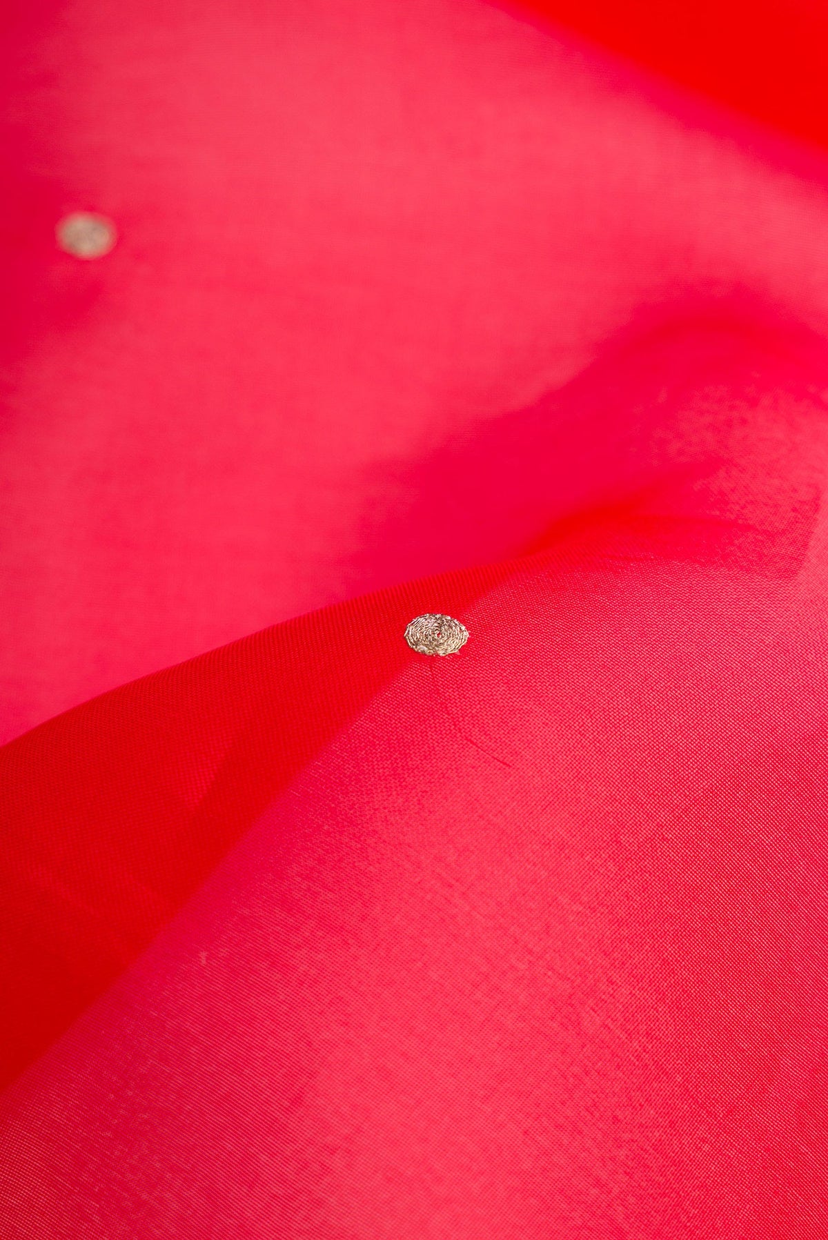 Close up of Red Dual Tone Organza Silk Saree with Zari Butta on the body and Embroidery Border.  displaying folds