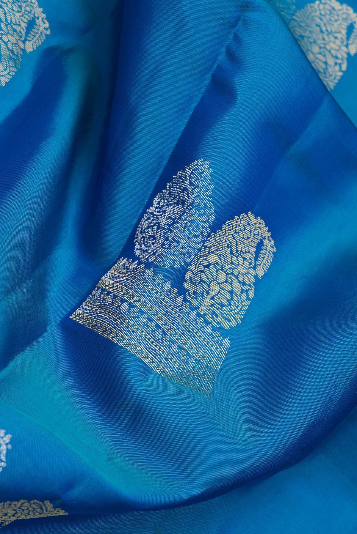 Close up of Peacock Blue Dual Tone Kanchipuram Silk Saree with Zari Butta on the body and Zari Border.  displaying folds