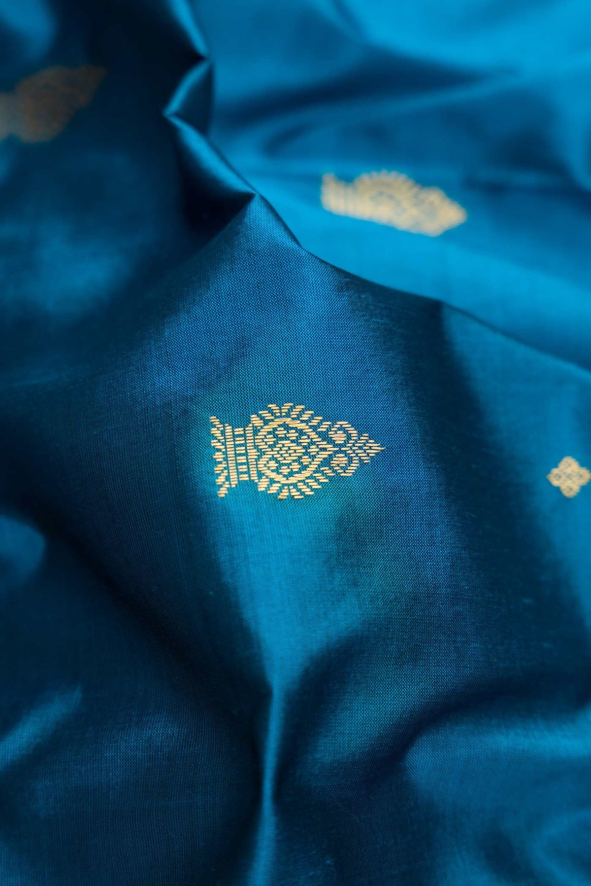 Close up of Peacock Blue Dual Tone Kanchipuram Silk Saree with Zari Butta on the body and Temple Border.  displaying folds