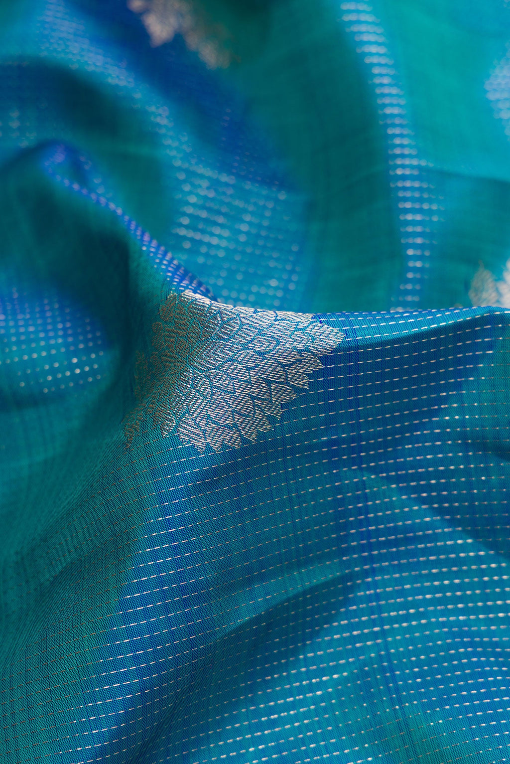 Close up of Peacock Blue Dual Tone Kanjivaram Silk Saree with Zari Butta on the body and Zari Border.  displaying folds