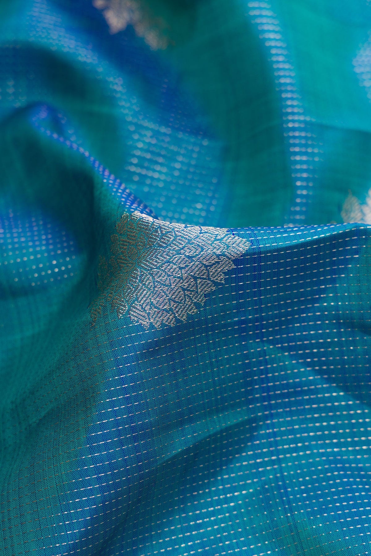 Close up of Peacock Blue Dual Tone Kanjivaram Silk Saree with Zari Butta on the body and Zari Border.  displaying folds