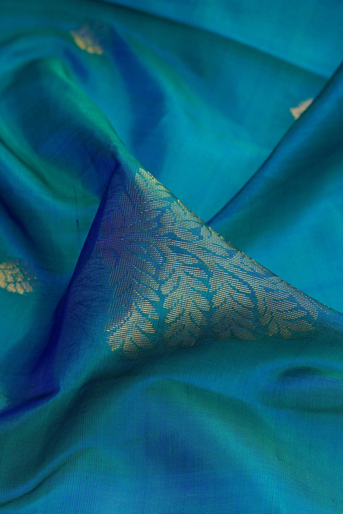 Close up of Peacock Blue Dual Tone Soft Silk Saree with Zari Butta on the body and Fancy Border.  displaying folds