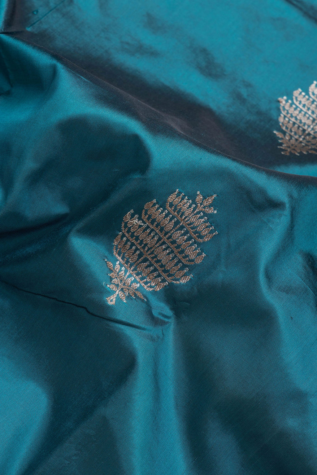 Close up of Peacock Blue Dual Tone Banarasi Silk Saree with Zari Butta on the body and Thread Border.  displaying folds