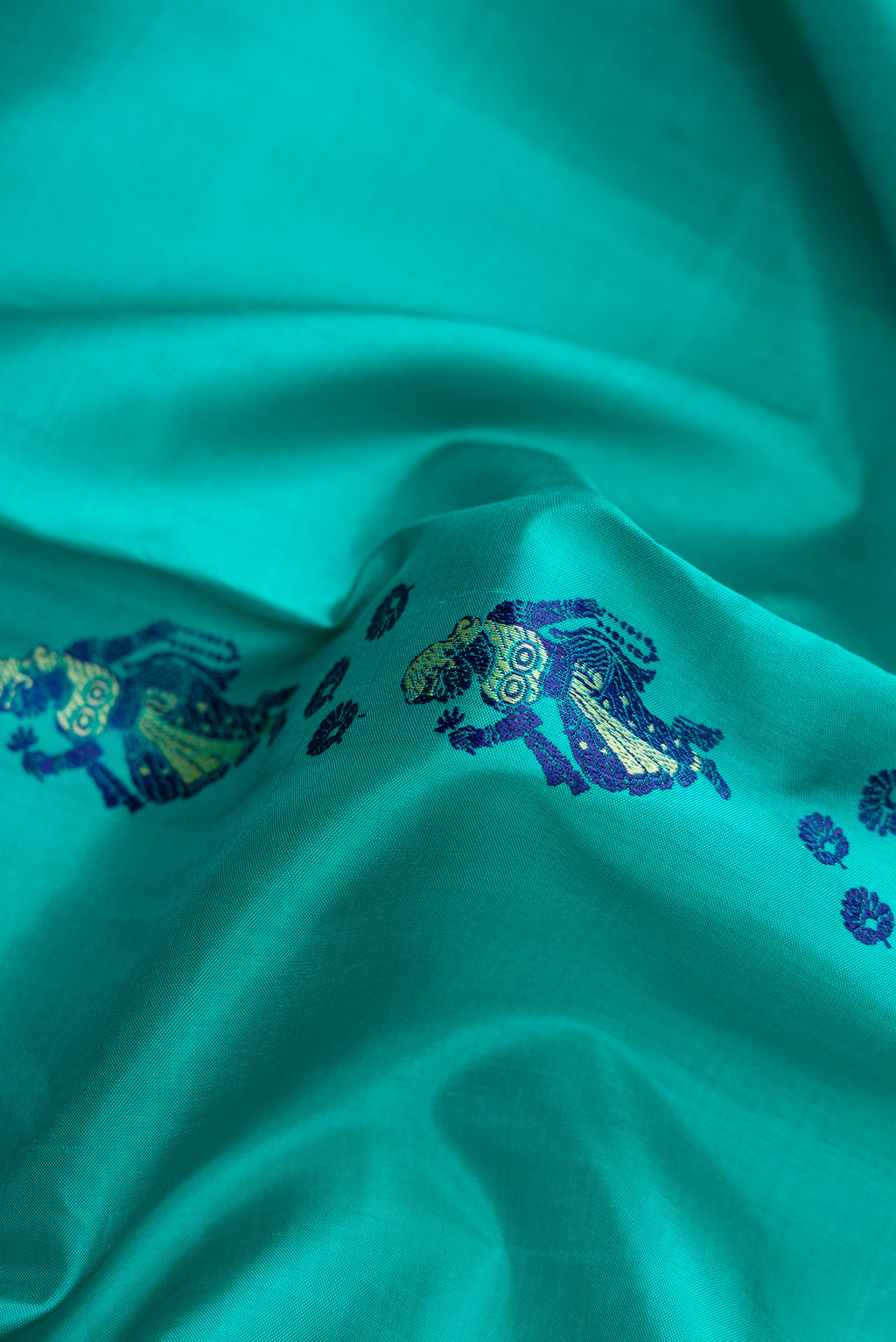 Close up of Turquoise Baluchari Silk Saree with Thread Butta on the body and Thread Border.  displaying folds