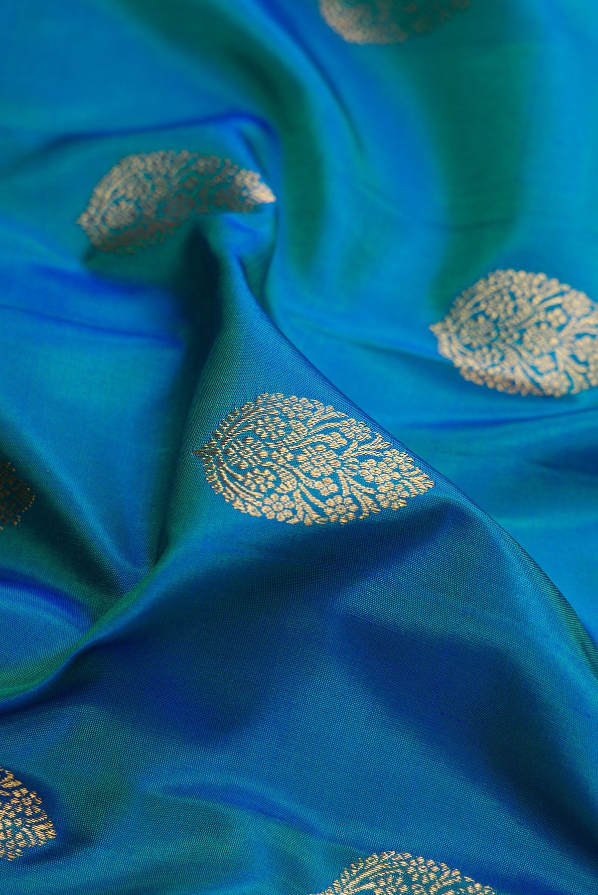Close up of Pure Silk Pure Zari Peacock Blue Dual Tone Kanjivaram Saree with Zari Butta on the body and Zari Border.  displaying folds