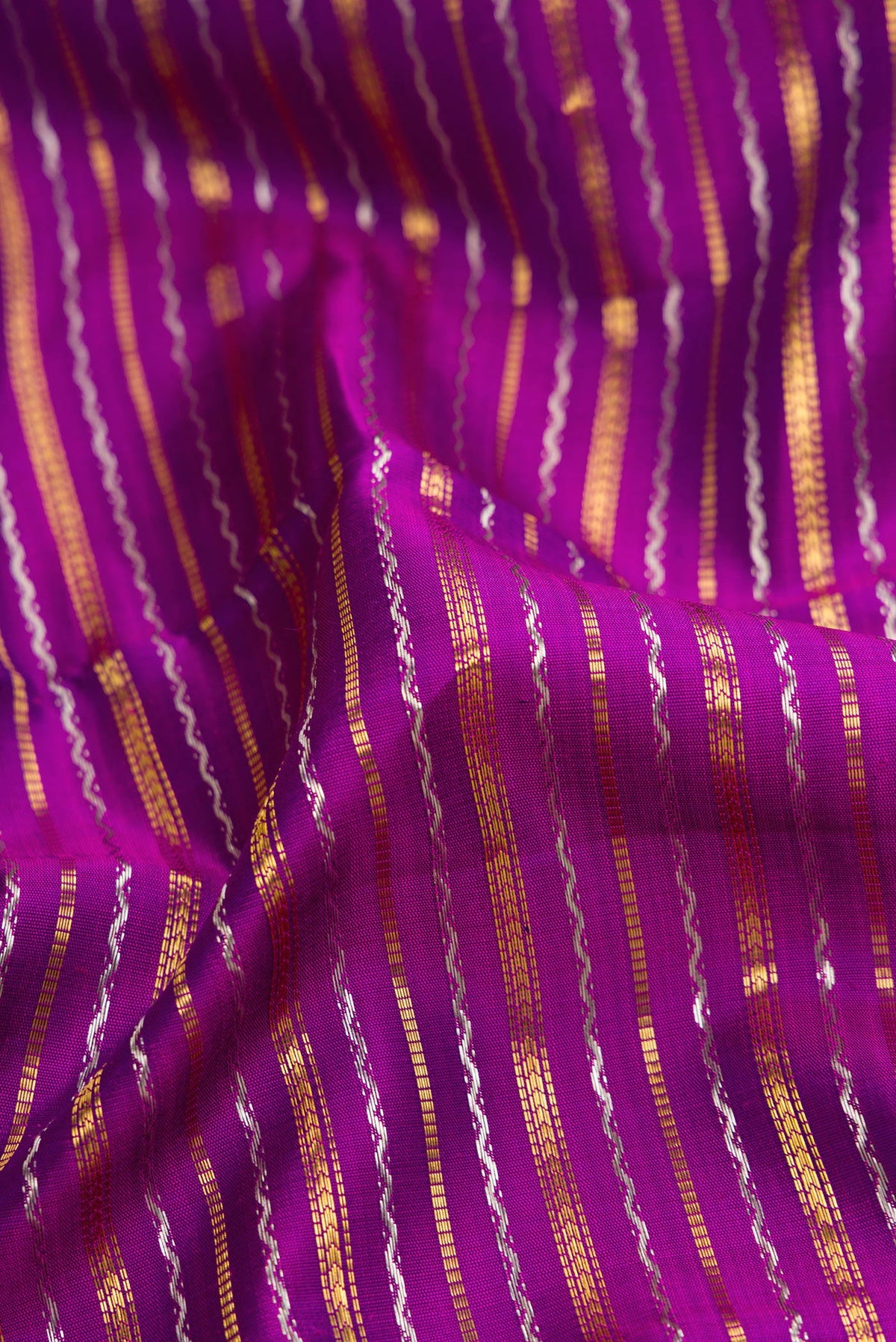 Close up of Magenta Dual Tone Kanchipuram Silk Saree with Stripes on the body and Zari Border.  displaying folds