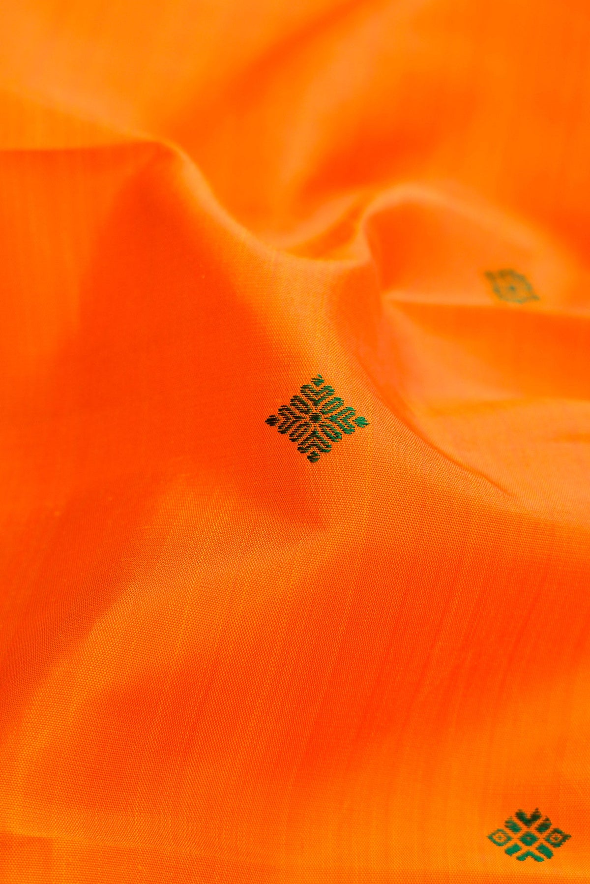 Close up of Pure Silk Pure Zari Orange Dual Tone Kanchipuram Saree with Thread Butta on the body and Zari Border.  displaying folds
