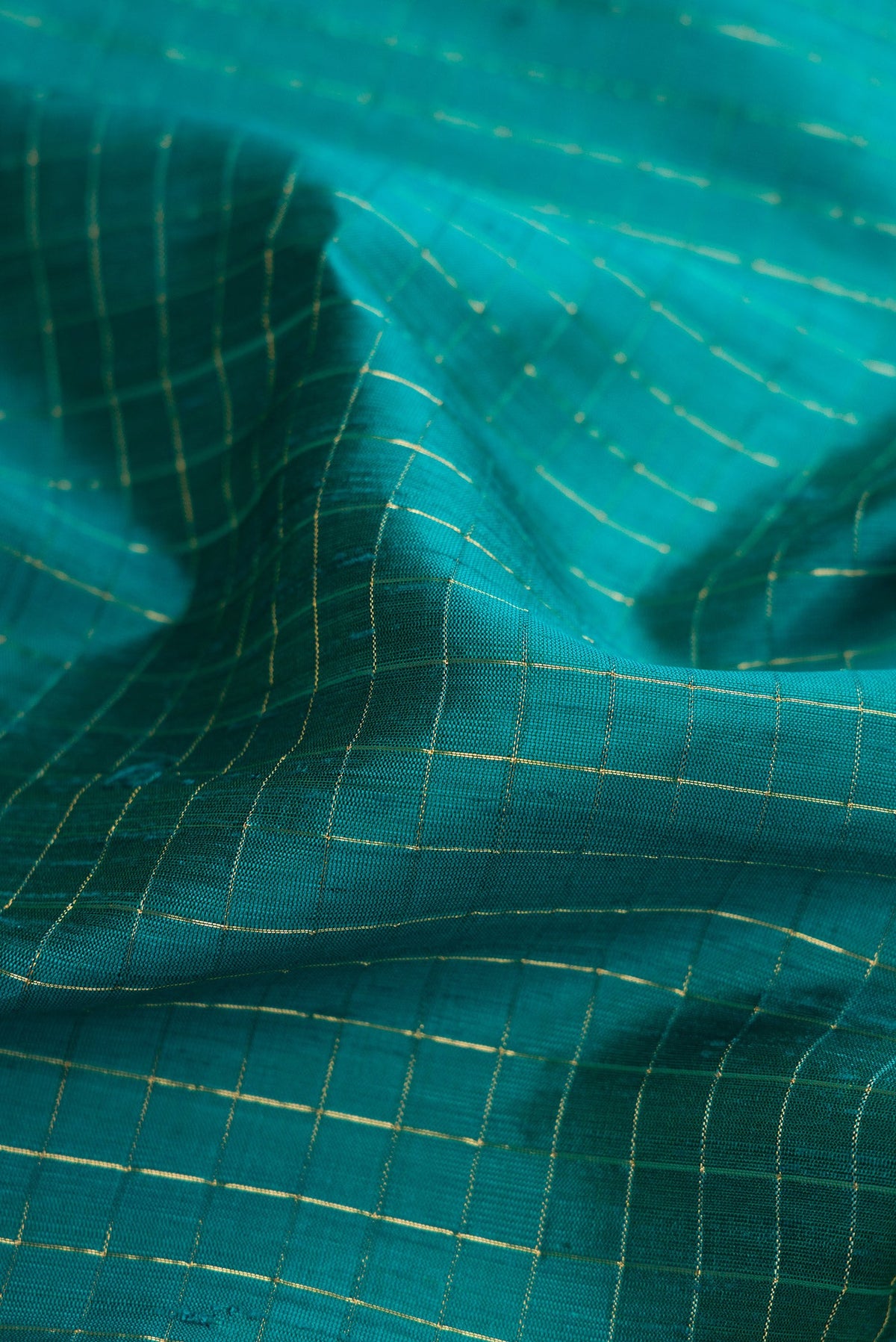 Close up of Peacock Blue Raw Silk Saree with Checked design on the body and Zari Border.  displaying folds