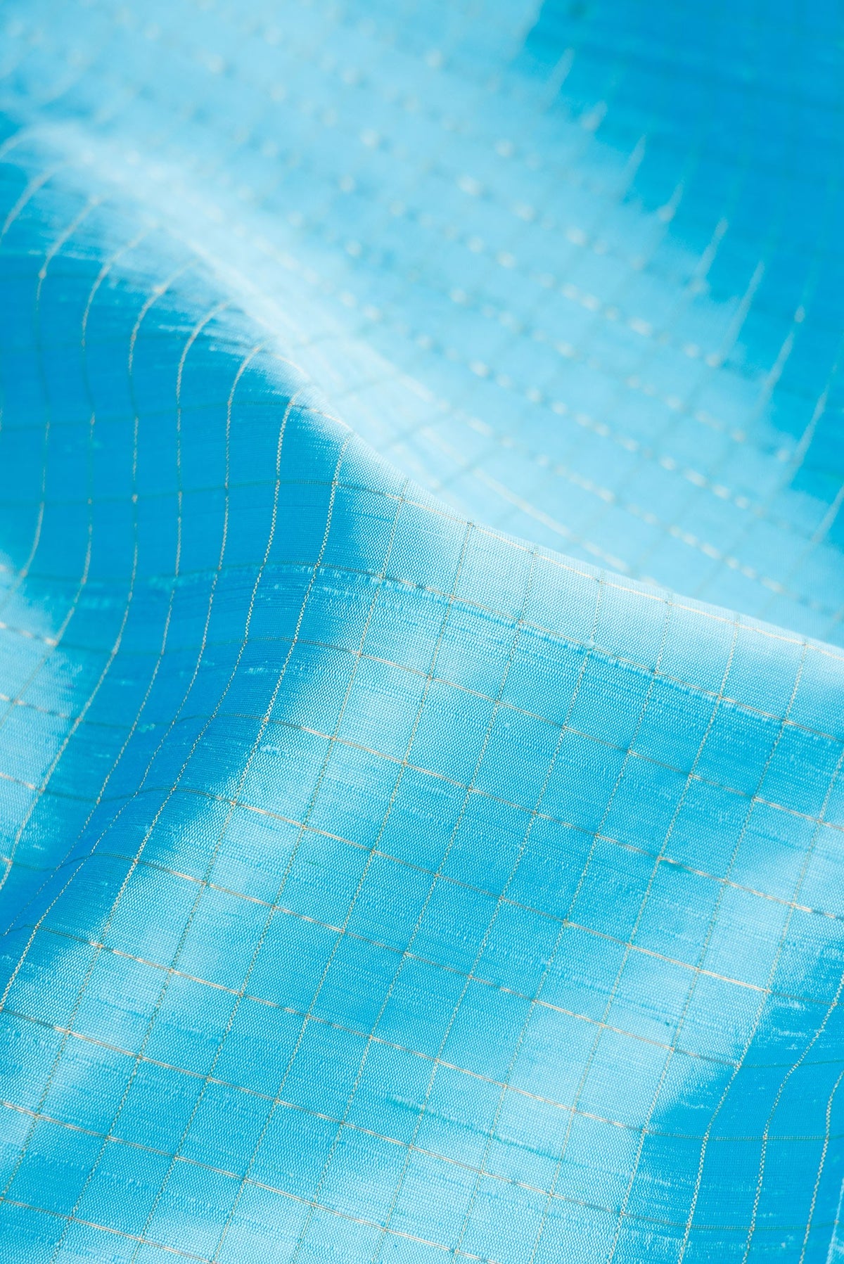 Close up of Sky Blue Raw Silk Saree with Checked design on the body and Zari Border.  displaying folds