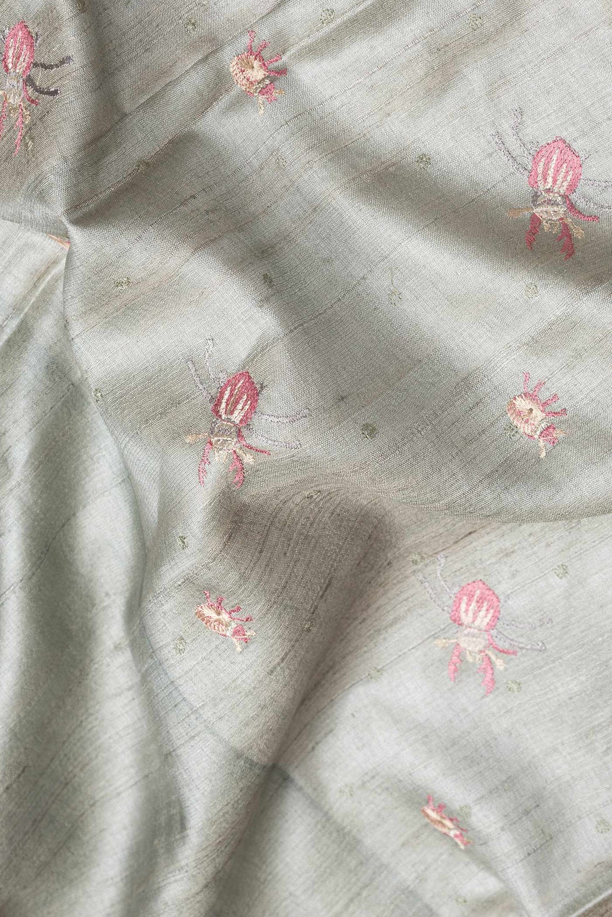 Close up of Grey Dual Tone Tussar Silk Saree with Thread Butta on the body and Embroidery Border.  displaying folds