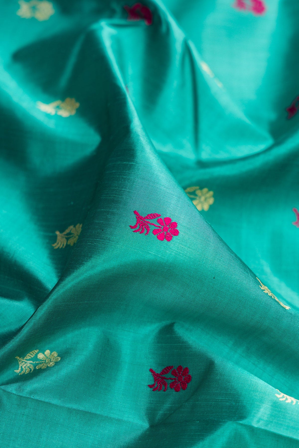 Close up of Turquoise Baluchari Silk Saree with Thread Butta on the body and Thread Border.  displaying folds
