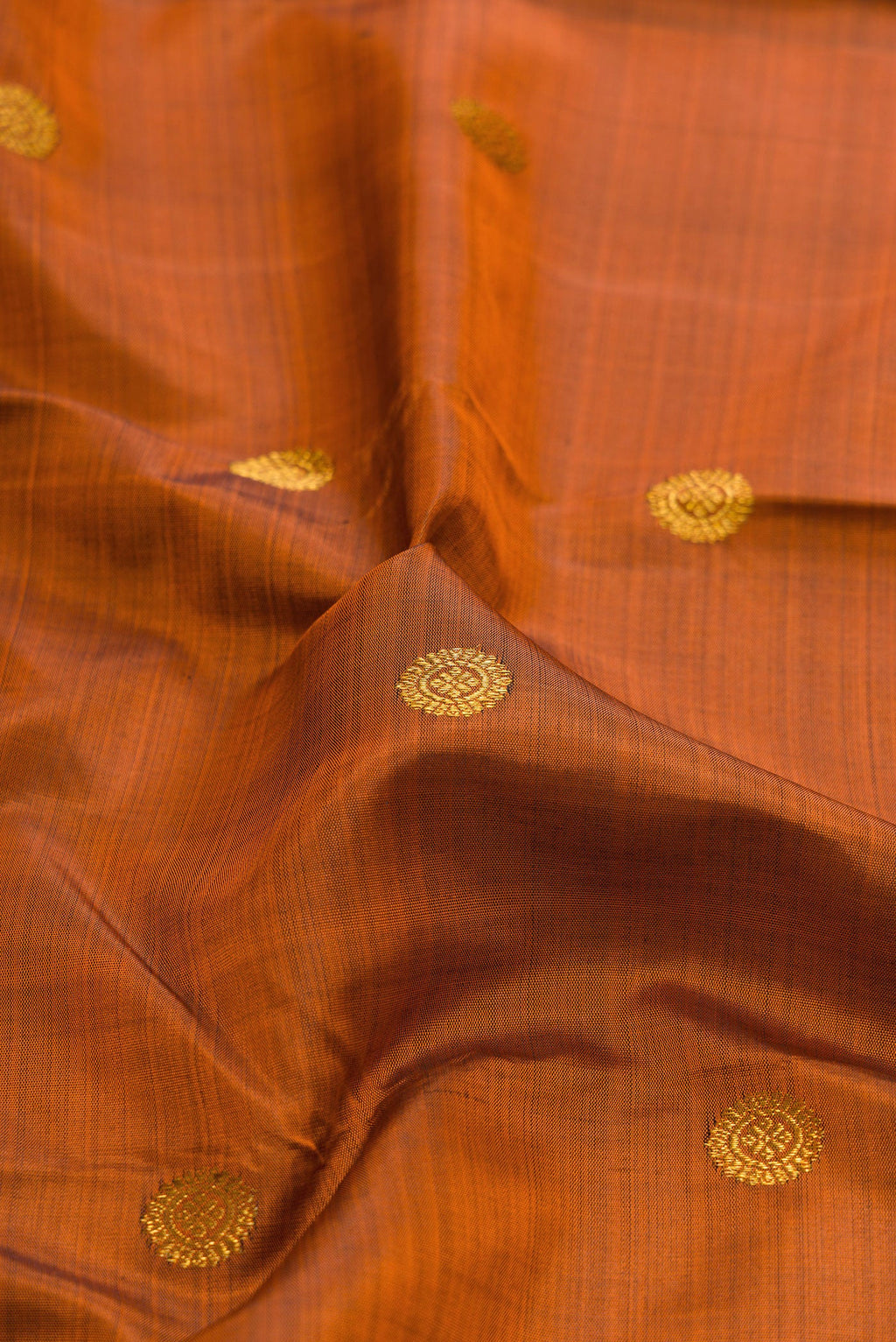 Close up of Rust Kanjivaram Silk Saree with Zari Butta on the body and Zari Border.  displaying folds
