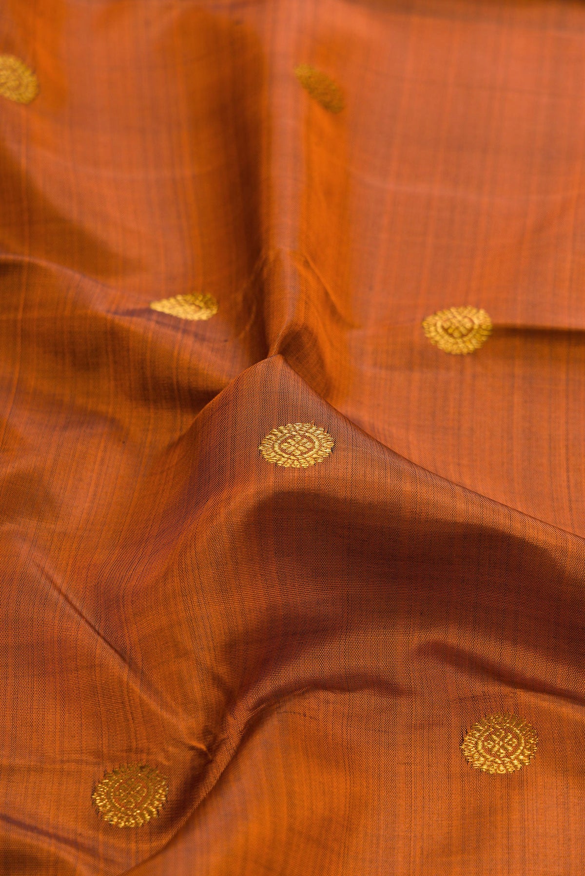 Close up of Rust Kanjivaram Silk Saree with Zari Butta on the body and Zari Border.  displaying folds